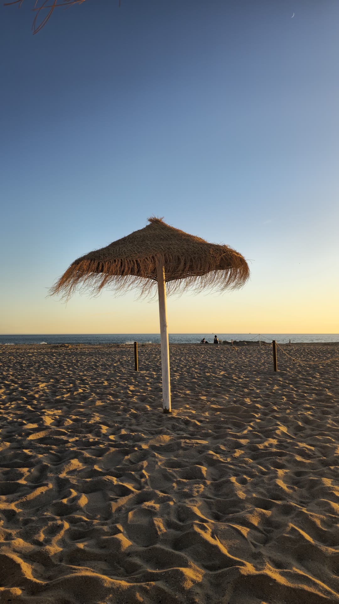 Guarda-sol de palha na Praia de Santo António ao entardecer, Costa da Caparica