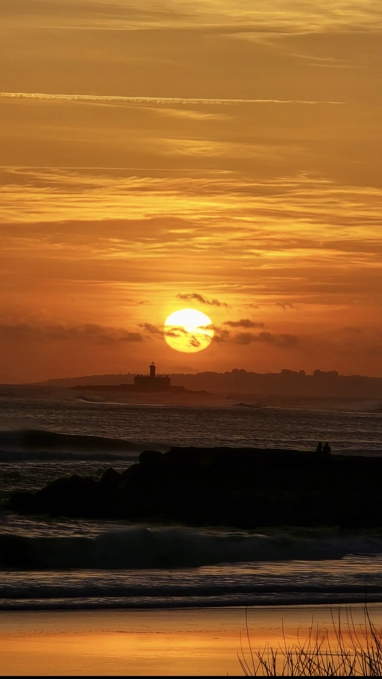 Pôr do sol sobre o mar com o farol do Abugiu